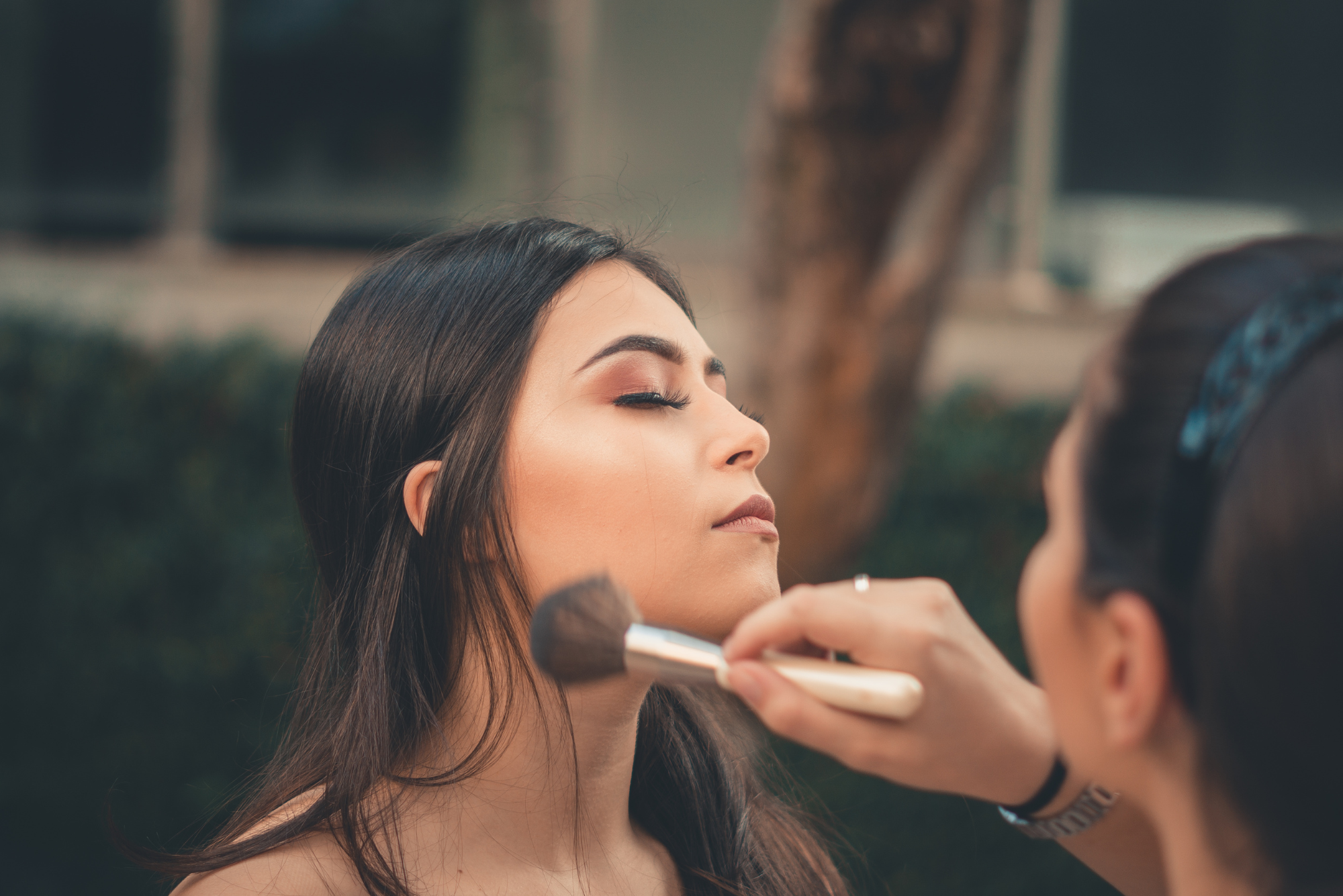 A close-up of a woman getting makeup applied with a brush.