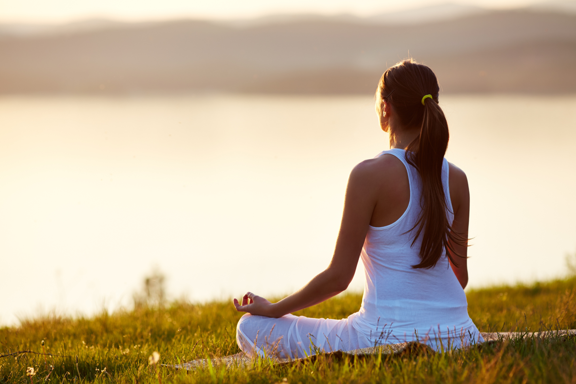 Woman meditating near a lake at sunset, symbolizing calm and balance for nervous system regulation and better health.