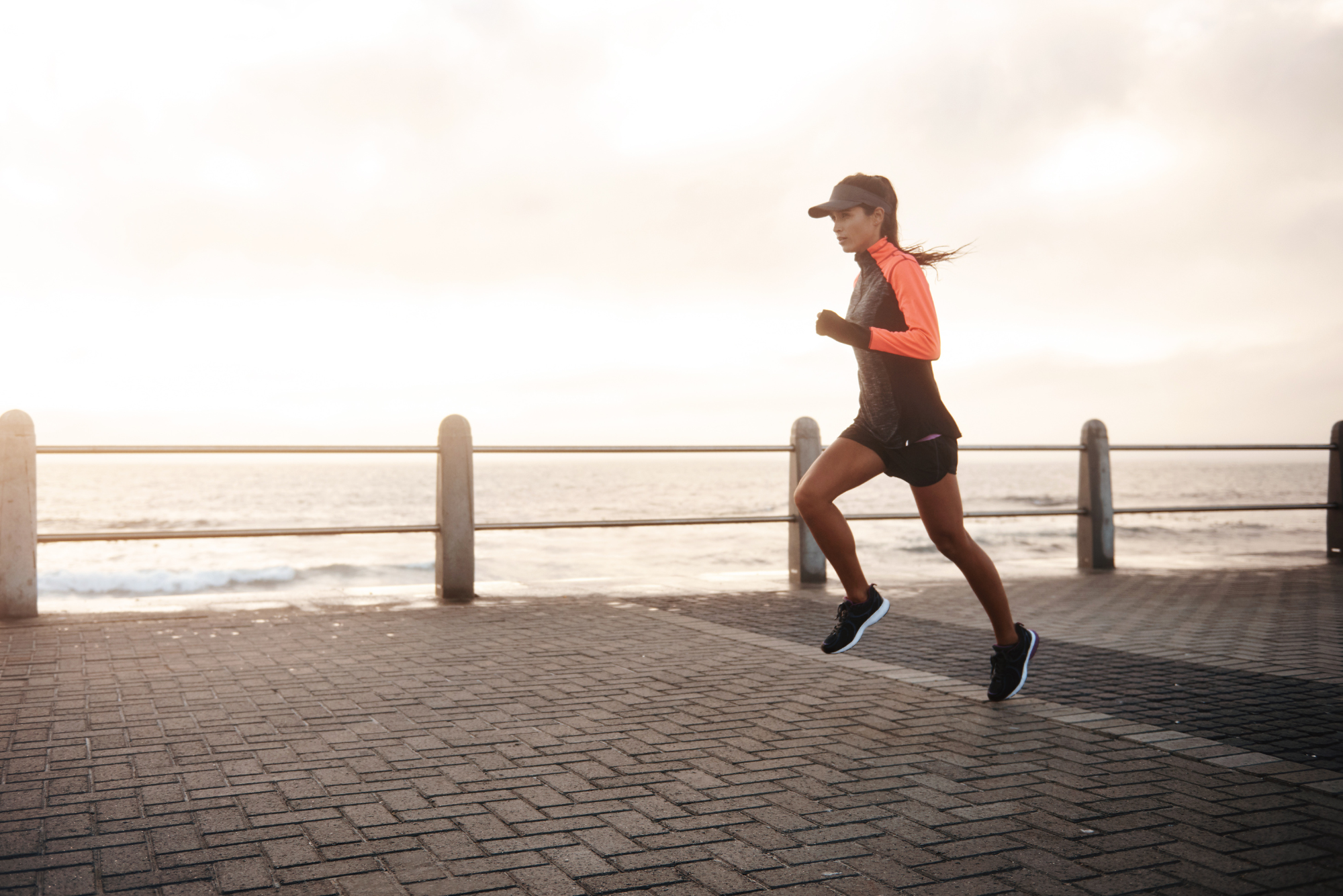 A woman running along a seaside promenade at sunrise, embracing a holistic approach to wellness by learning how to naturally lower cortisol.