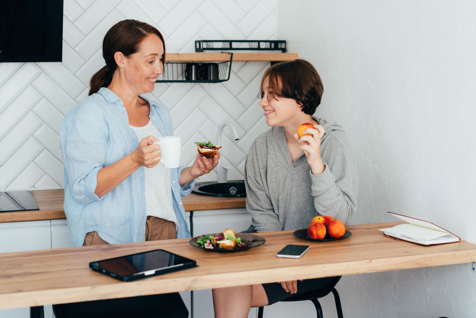 Mother and daughter enjoy healthy snacks while chatting in kitchen.