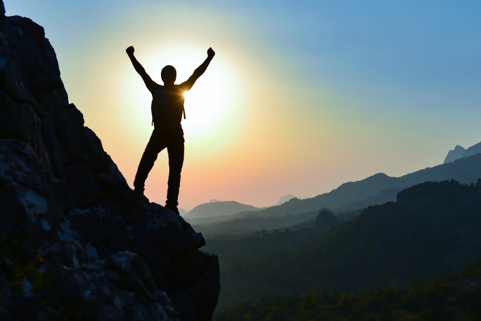 Silhouette of a person on a mountain peak with arms raised, symbolizing achieving success.